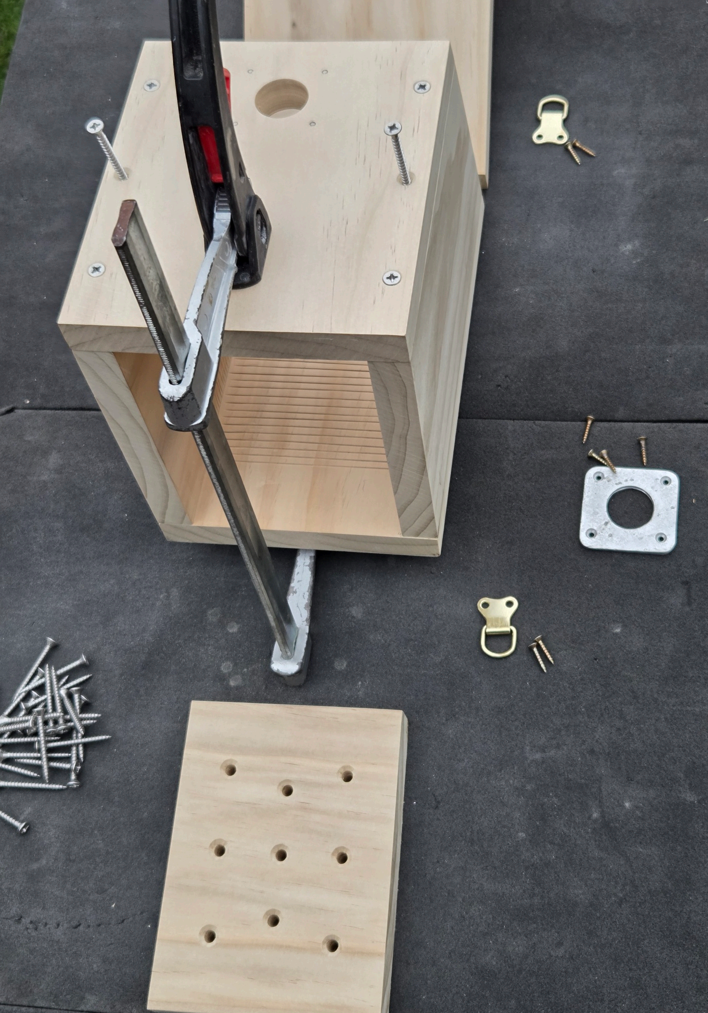 Wooden box frame being held together with a clamp, screws and hardware laid out nearby